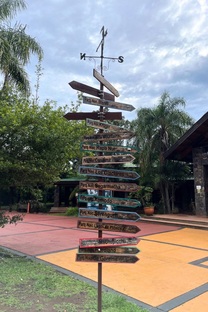 Wooden signpost with arrows pointing to national parks worldwide, including Banff, Serengeti, and Komodo
