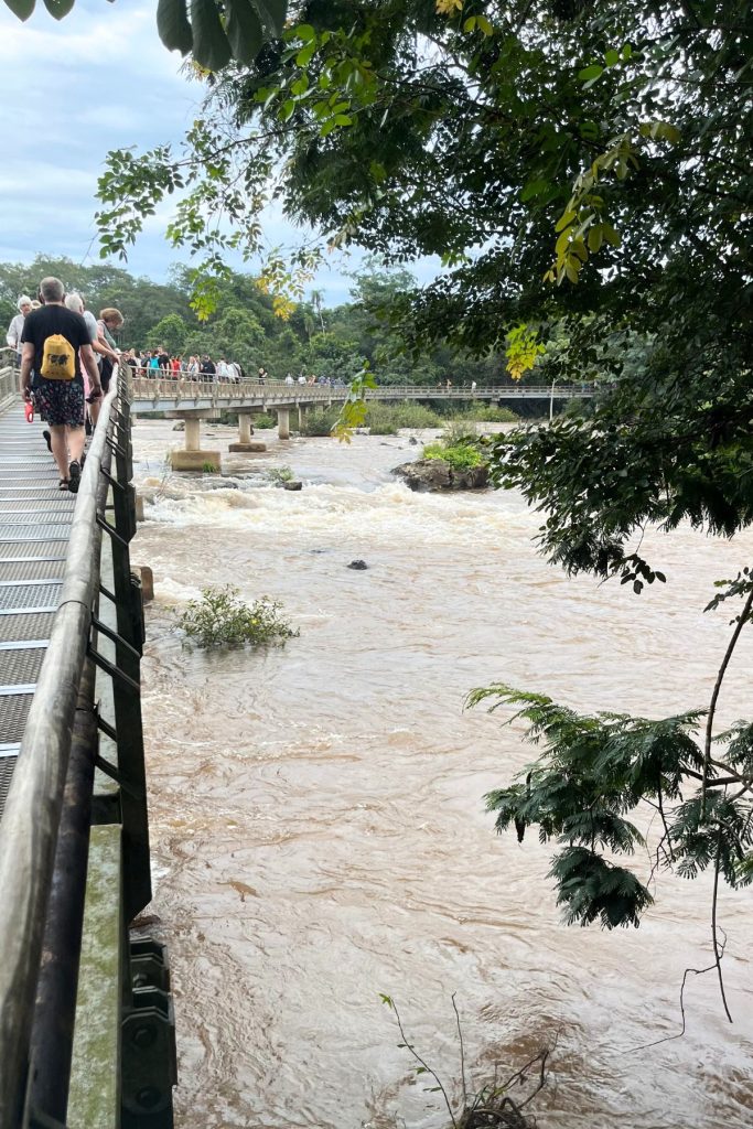 Visitors on a metal walkway beside a second bridge crossing a wide brown river