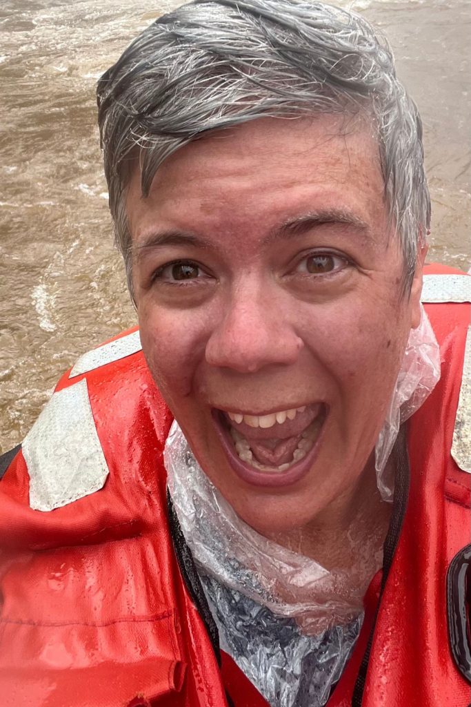 A woman with wet hair and mouth open in a shout, in a soaked life jacket on the boat