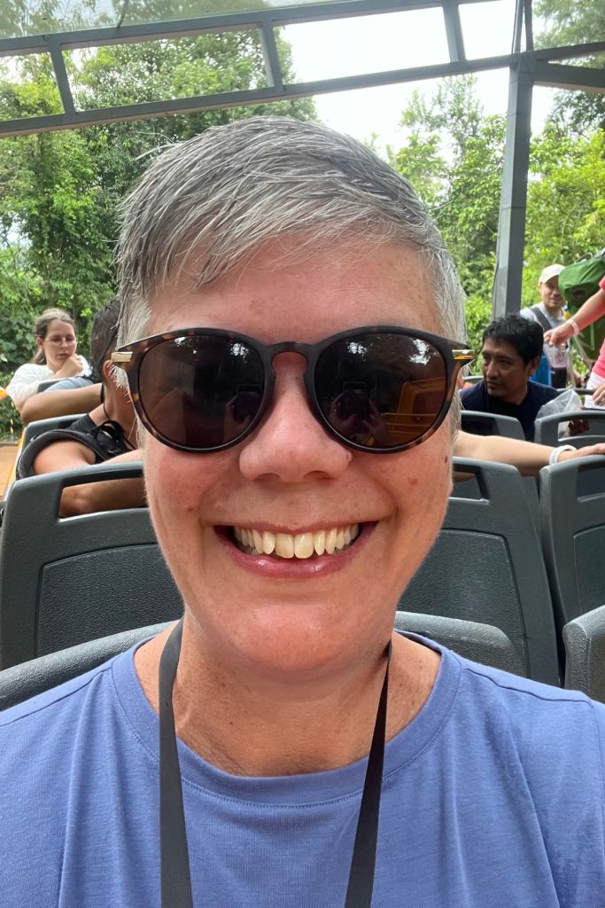 A woman in sunglasses and a blue shirt smiling in a 4x4 truck with other passengers behind her