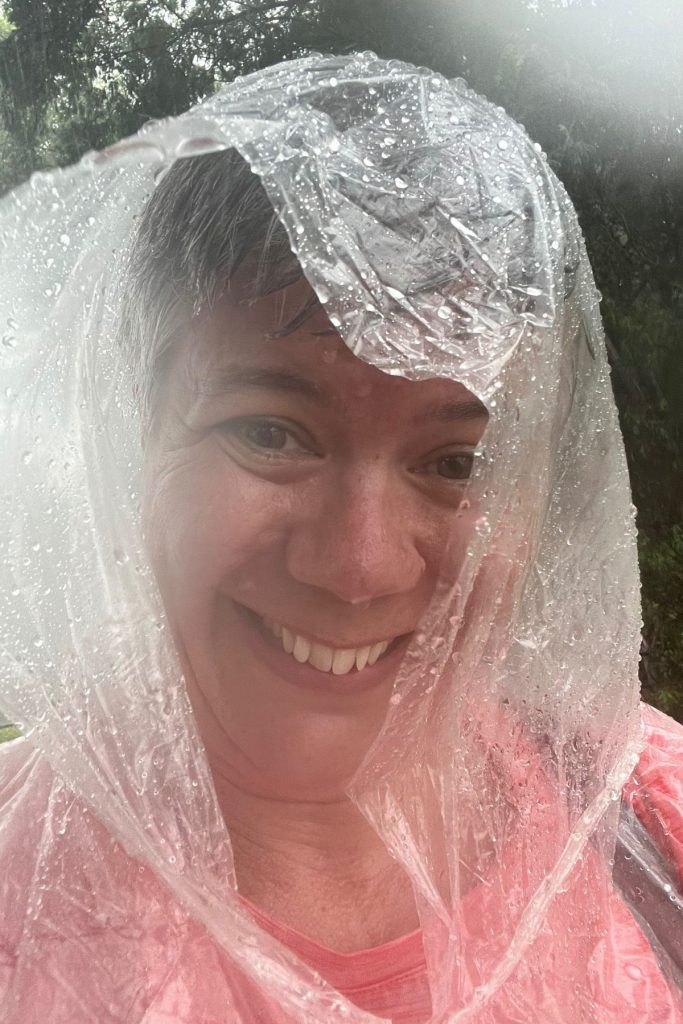 A smiling woman in a clear plastic poncho hood covered in raindrops