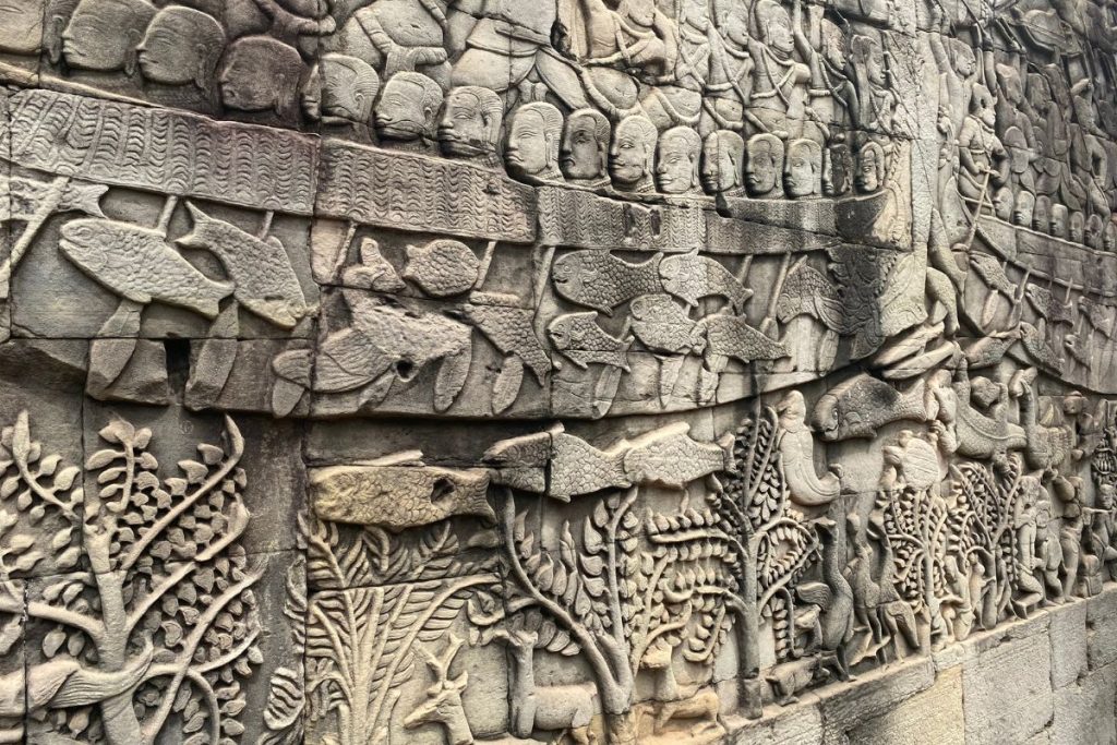 Stone bas-relief of a boat with a row of heads above large fish, with trees and a deer carved below.