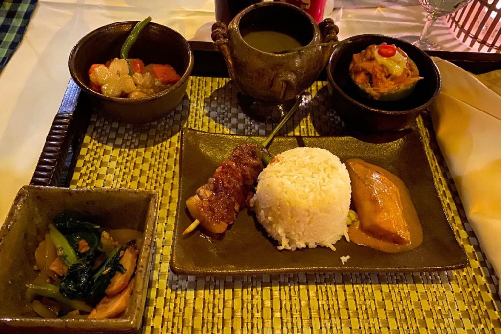 Tray with a mound of rice, a grilled skewer, a portion in golden curry sauce, and small bowls of vegetables and soup.