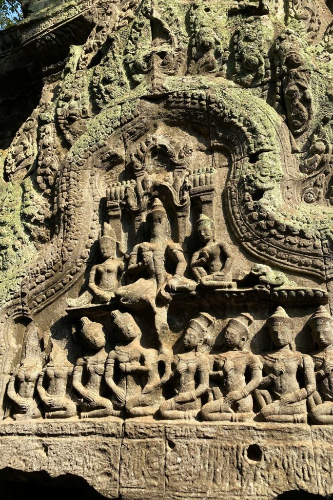 Stone carving of seated figures beneath a decorated arch, covered in green lichen.