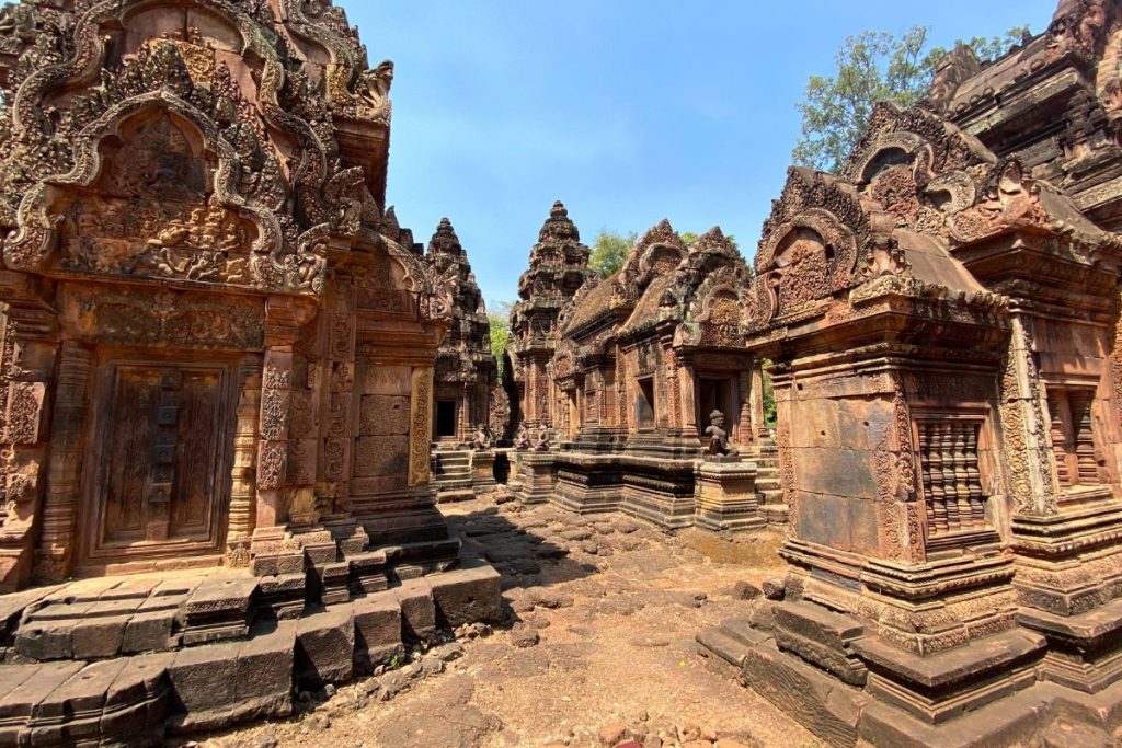 Narrow courtyard between carved red sandstone shrines with decorated pediments and small guardian figures at the base of the steps.