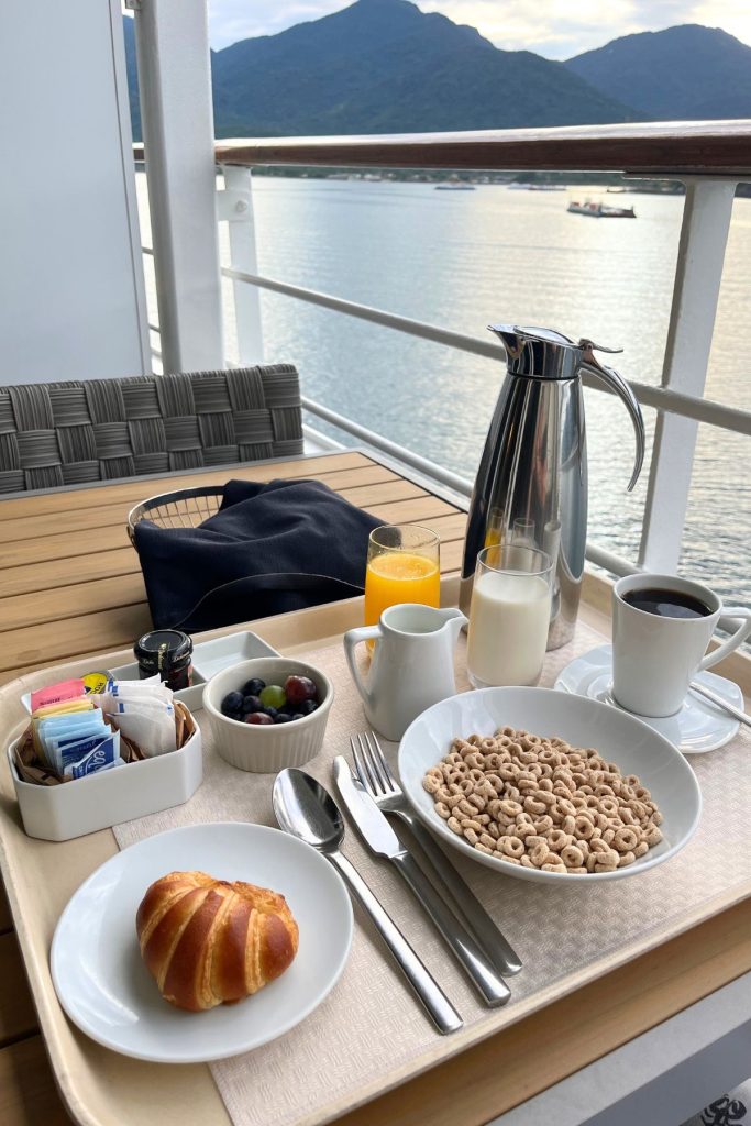 A tray of breakfast foods is sitting on a wooden table on a balcony on a cruise ship