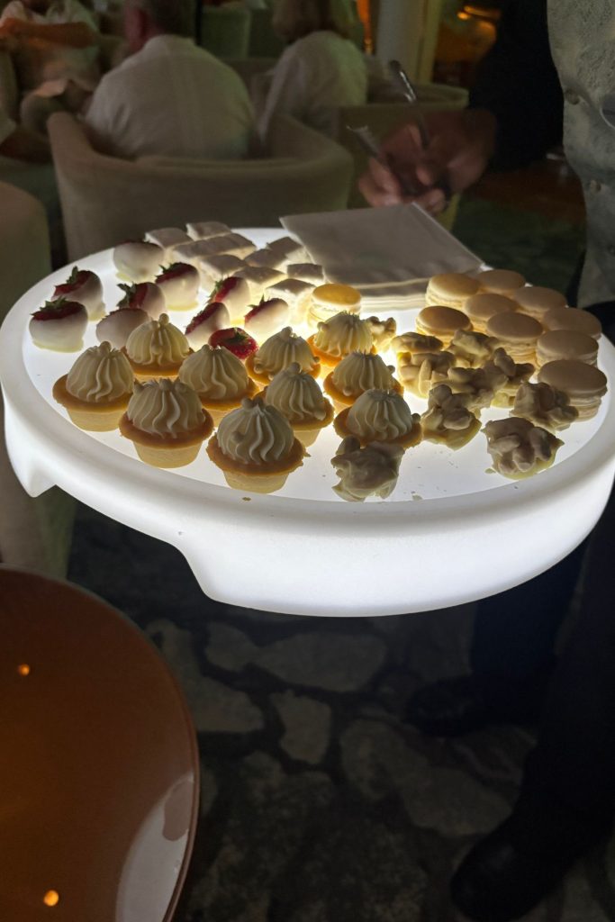 A white serving platter, lit up with white lights, holds many small appetizers and desserts, all of which are white colored.