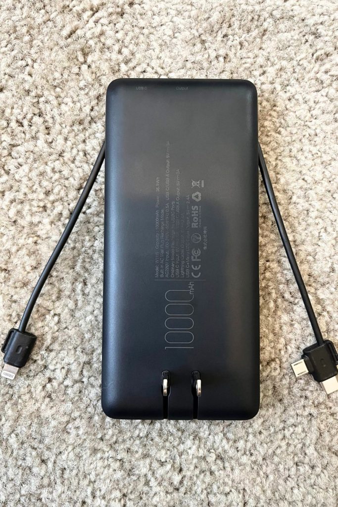 The underside of a black portable power bank is shown, with two built-in lightning cables extended - one on the left and one on the right.
