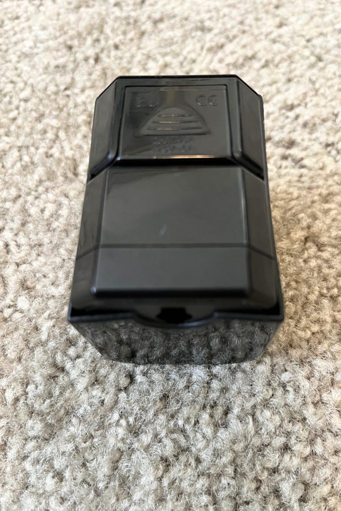 The underside of a shiny, rectangular, black plastic case with a thumb grip to slide the top section open shown.