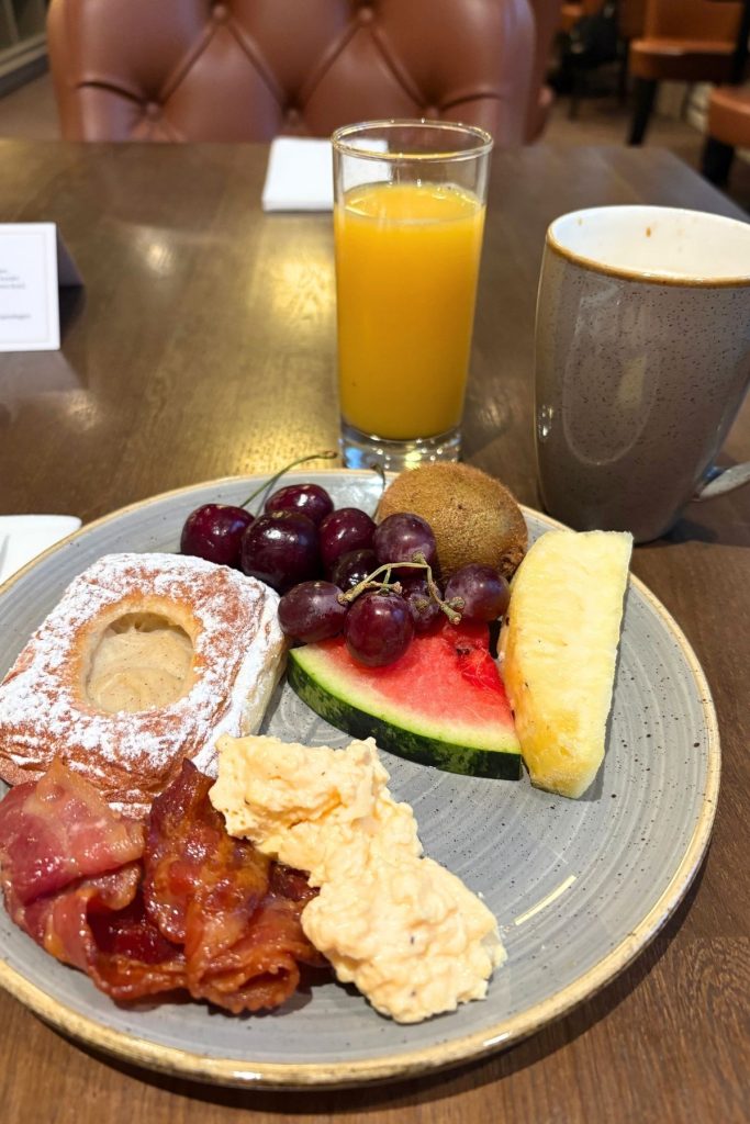 A blue plate sitting on a wooden table is filled with breakfast food, with a glass of orange juice and a gray mug of coffee behind it.
