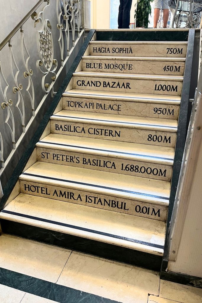 A set of beige marble stairs leading up, with the name of a famous Istanbul location (such as Hagia Sophia and Blue Mosque) and its distance in meters stamped on the riser of each step