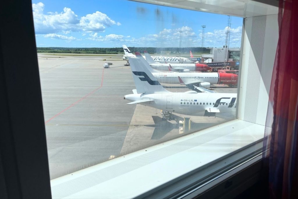 A row of four airplanes parked at gates, as seen from a window with a red curtain pulled to the right side.