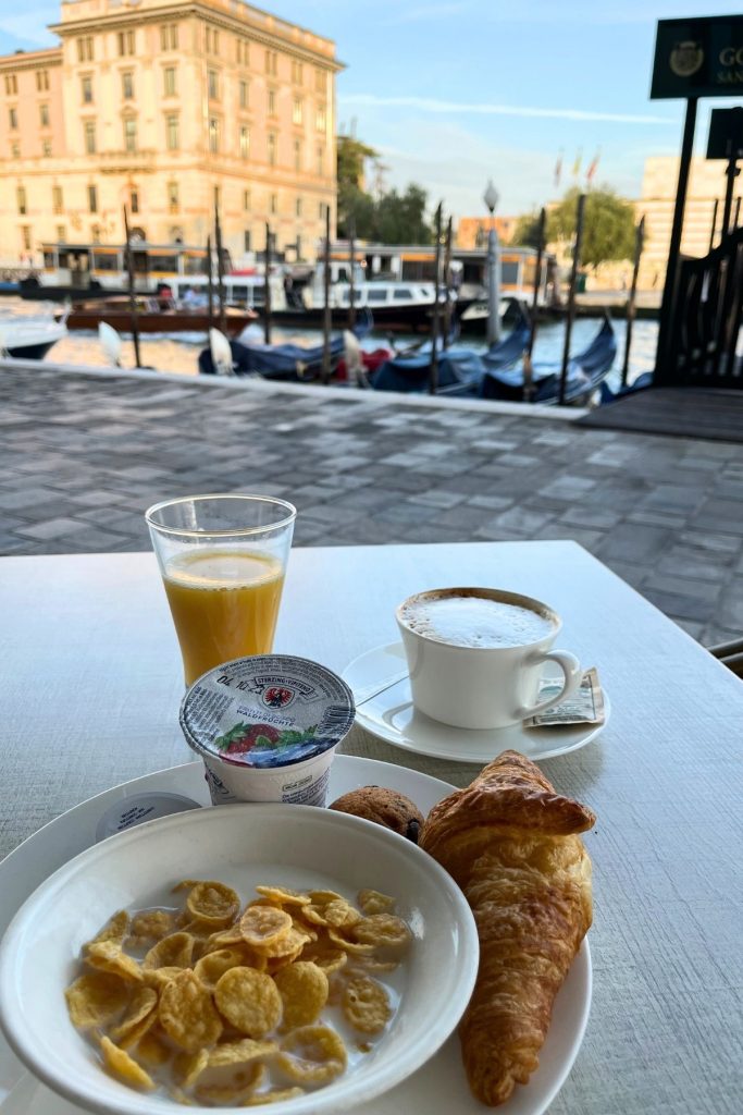 A white plate sitting on a wooden table is filled with breakfast food, with a glass of orange juice and a white mug of coffee behind it.