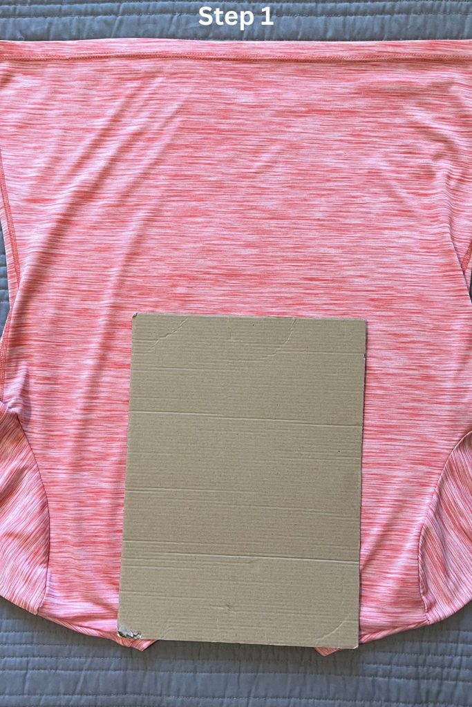 An orange tee shirt is laid out, with a smaller rectangular piece of brown cardboard on top at the neck opening.