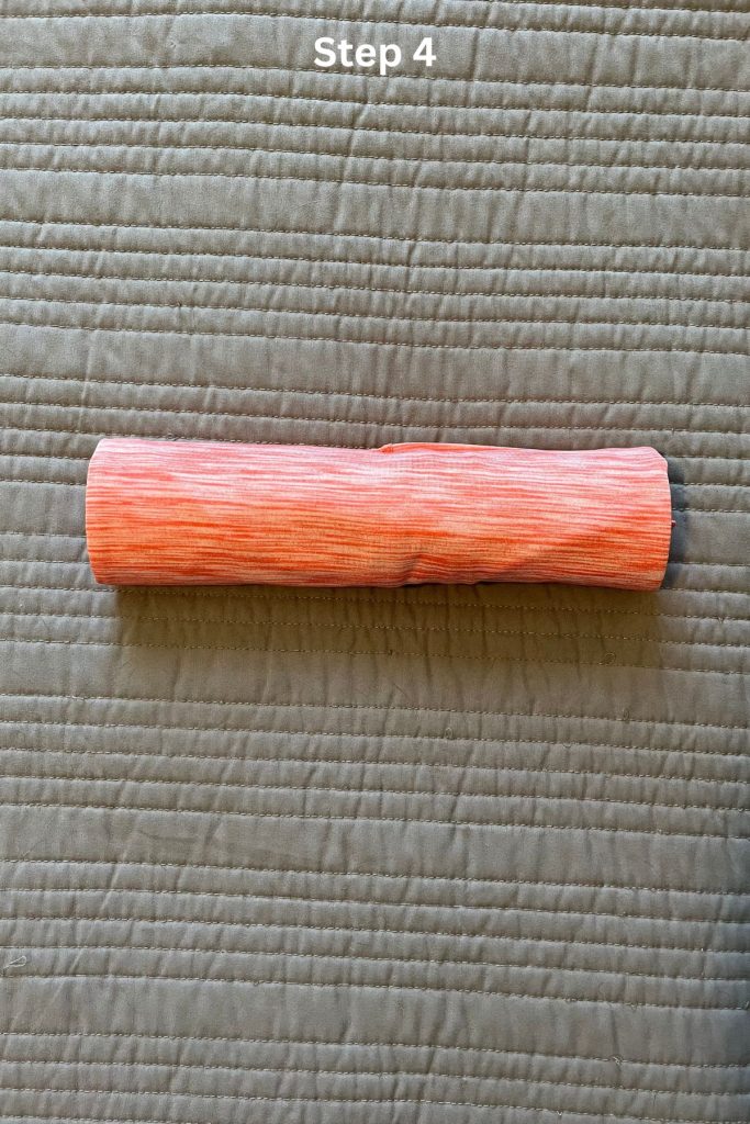 An orange tee shirt, rolled up, sits on a gray background