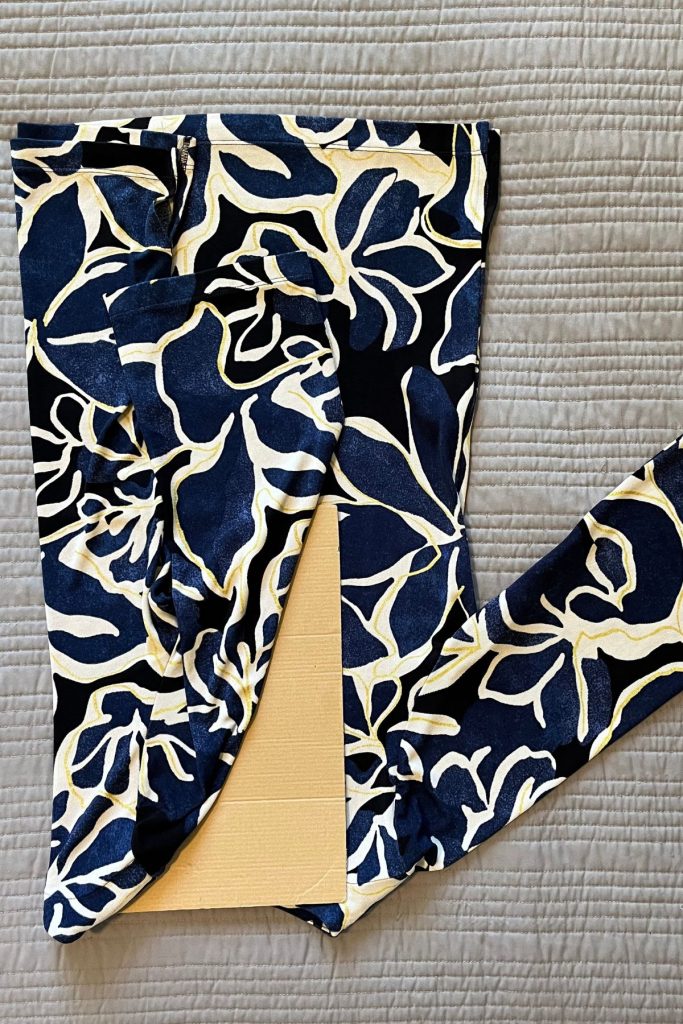 A black, blue, and cream colored pattered shirt is laid out, with the left third folded lengthwise around a smaller rectangular piece of brown cardboard at the neck opening.