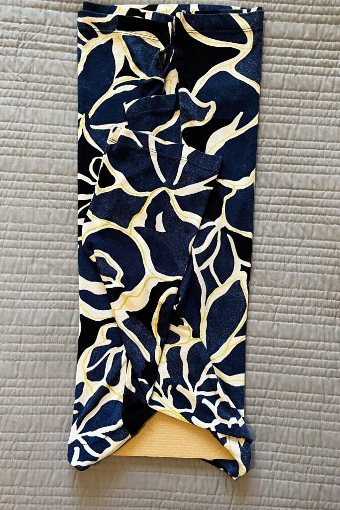 A black, blue, and cream colored pattered shirt is folded lengthwise in thirds around a smaller rectangular piece of brown cardboard at the neck opening.