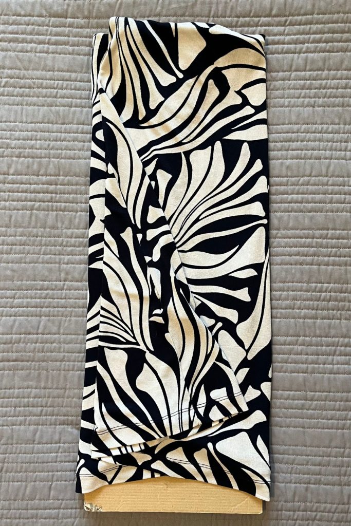 A black and white patterned dress is folded lengthwise in thirds around a smaller rectangular piece of brown cardboard at the neck opening.