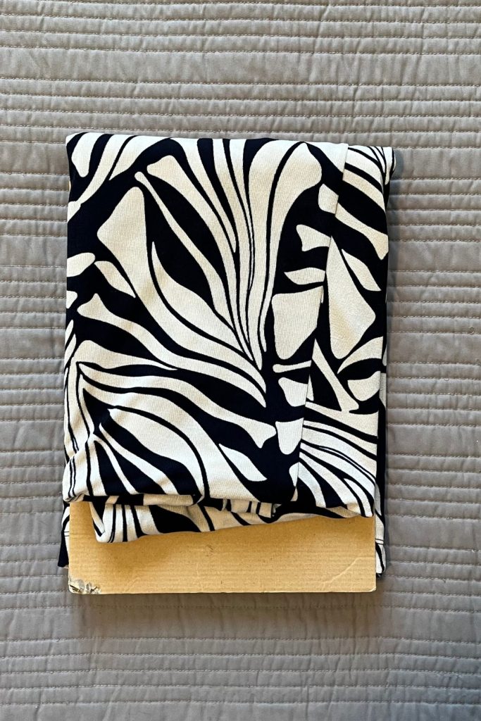 A black and white patterned dress is folded around a smaller rectangular piece of brown cardboard at the neck opening.