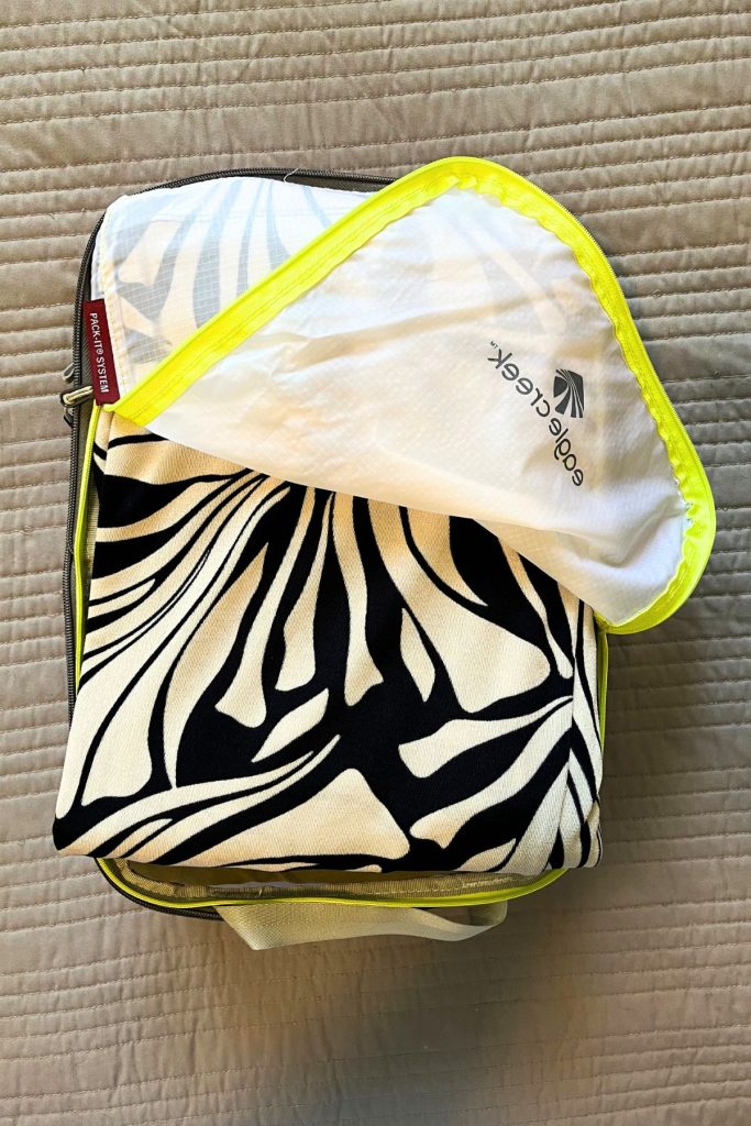 An open, white packing cube is filled with clothes, with a black and white patterned item seen at the top.