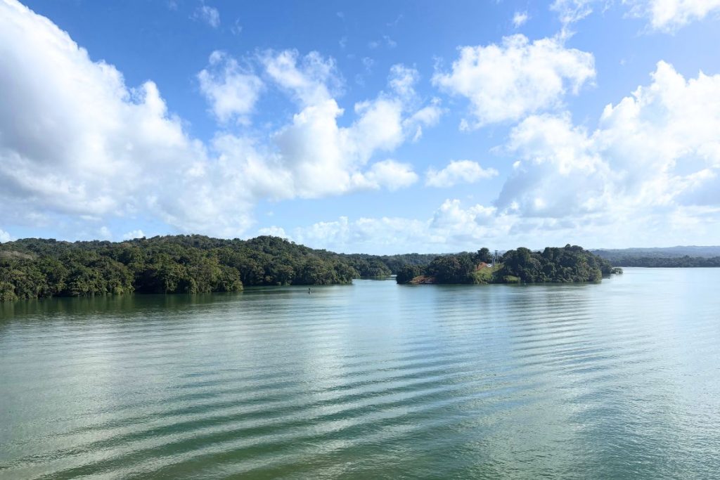 Forested islands on a calm green lake, with ripples from the ship's wake in the foreground