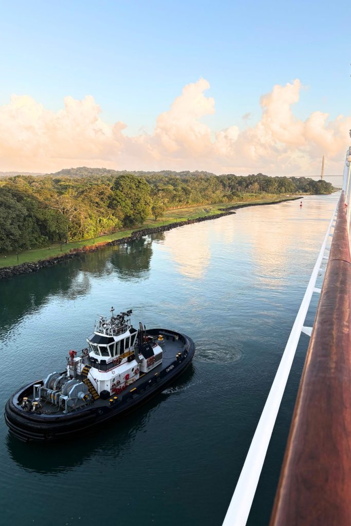 Black and white tugboat named Darién on calm water beside a wooded shoreline, with a bridge in the distance