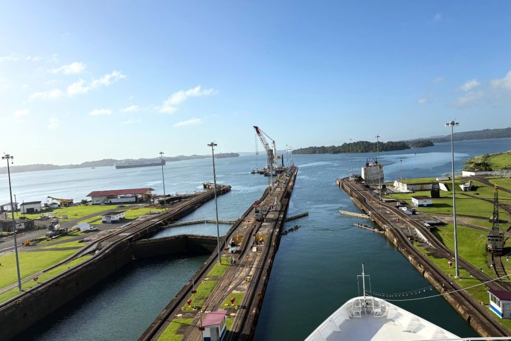 View from a ship's bow toward half-open lock gates, with the chamber full and Gatun Lake beyond