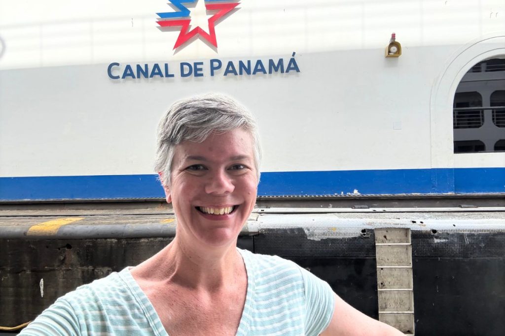 Smiling woman with short gray hair in a striped shirt in front of a white wall with the Canal de Panamá logo