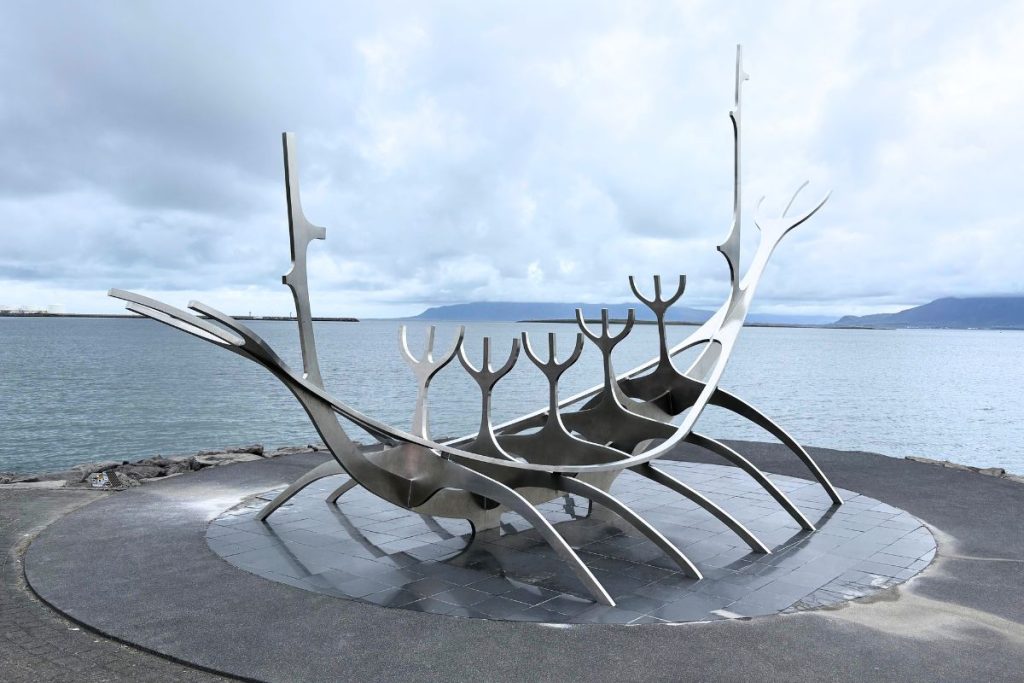 Steel Sun Voyager sculpture shaped like a Viking ship, with the bay and mountains behind