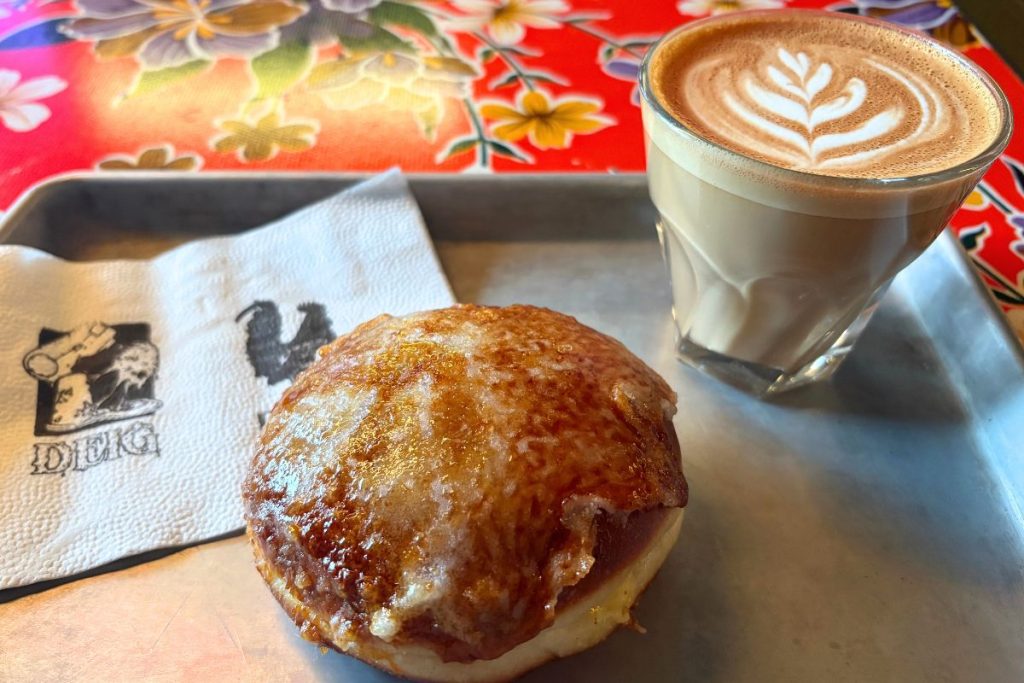 Creme brûlée donut and a latte with leaf foam art on a metal tray, with a DEIG napkin