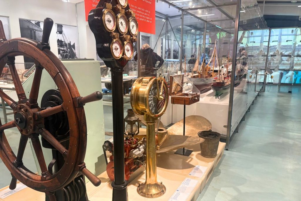 Ship's wheel, brass engine telegraph, and model ships in glass cases at a maritime museum
