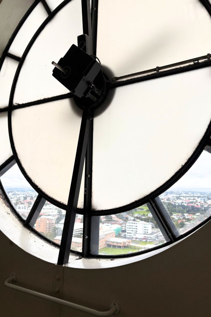 Back of a large tower clock face with Reykjavik visible through the gaps below