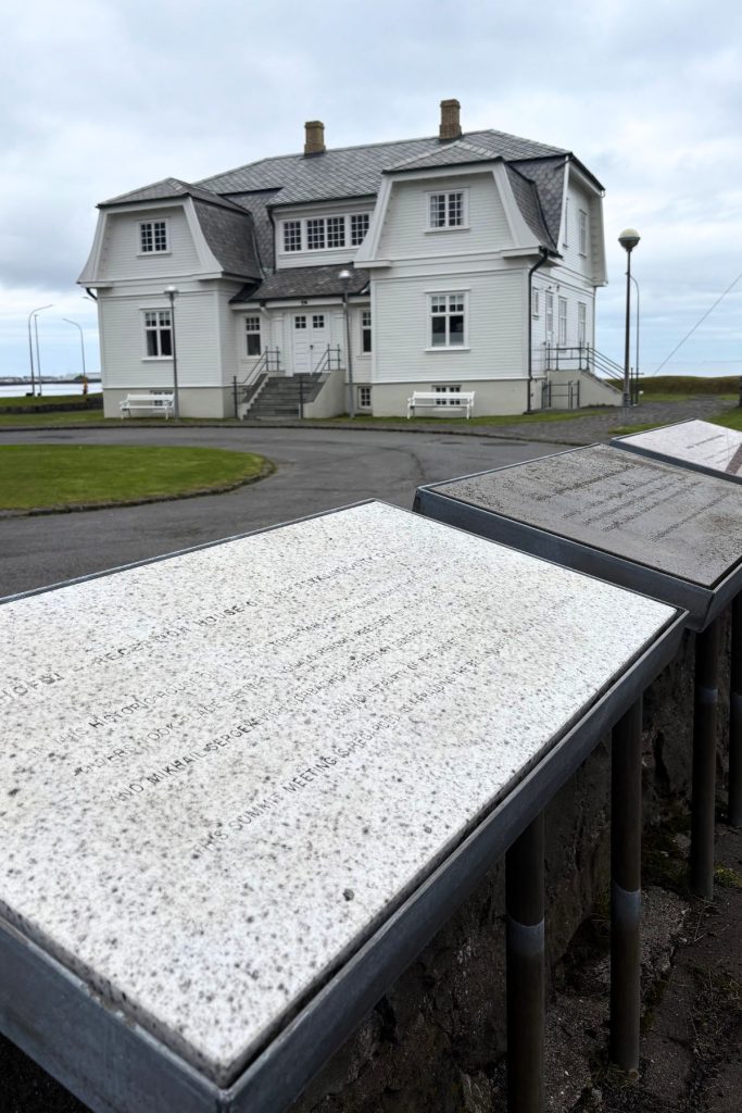 White two-story Höfði House near the waterfront, with stone plaques in the foreground