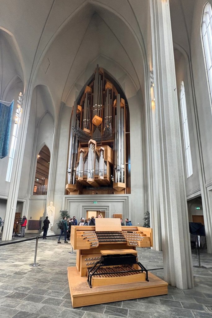 Tall gray arches and a pipe organ above a wooden organ console inside Hallgrímskirkja