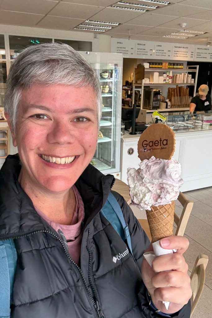 Smiling woman holding a cone of pink and white swirled gelato topped with a Gaeta wafer
