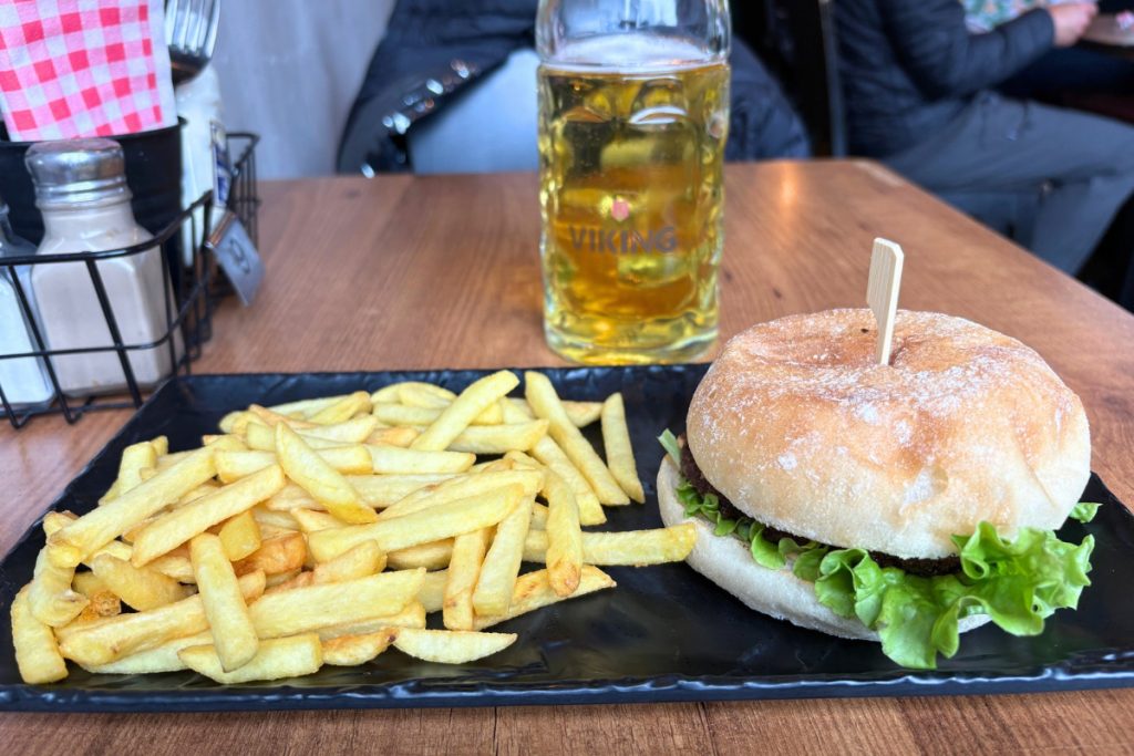 Burger on a floury bun and a pile of fries on a black plate, with a mug of Viking beer behind them