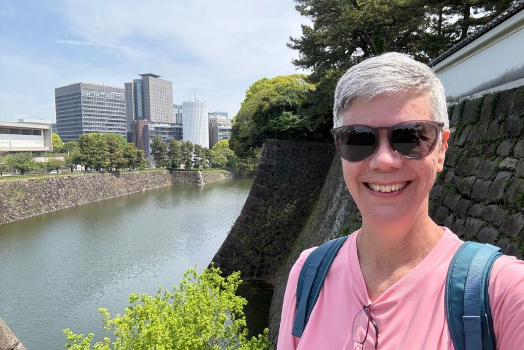 Woman smiling beside the moat and stone walls at the entrance to Imperial Palace East Gardens