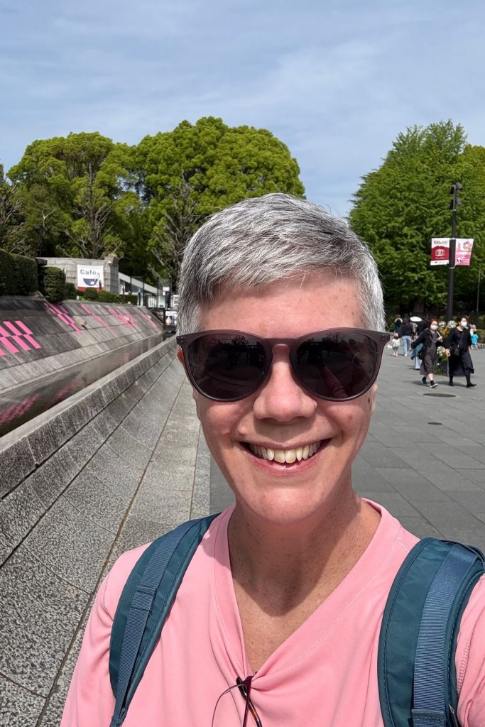 Woman smiling in Ueno Park with visitors walking along the path behind her