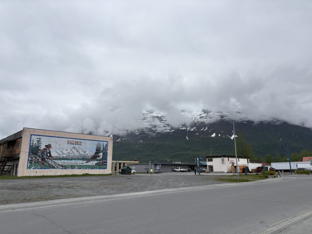 Mural of a gold rush prospector and eagle painted on a building in Valdez, Alaska, with mountains in the background