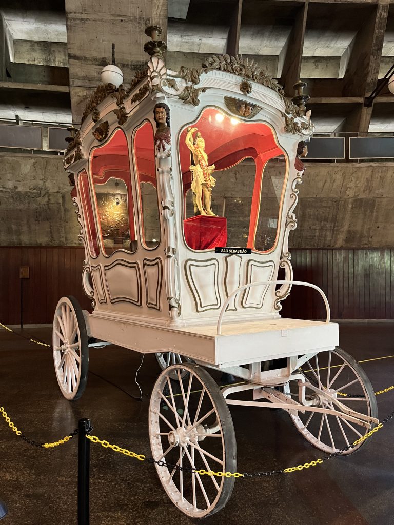 Ornate white and gold ceremonial carriage with a statue of São Sebastião, displayed inside the Metropolitan Cathedral of Rio de Janeiro