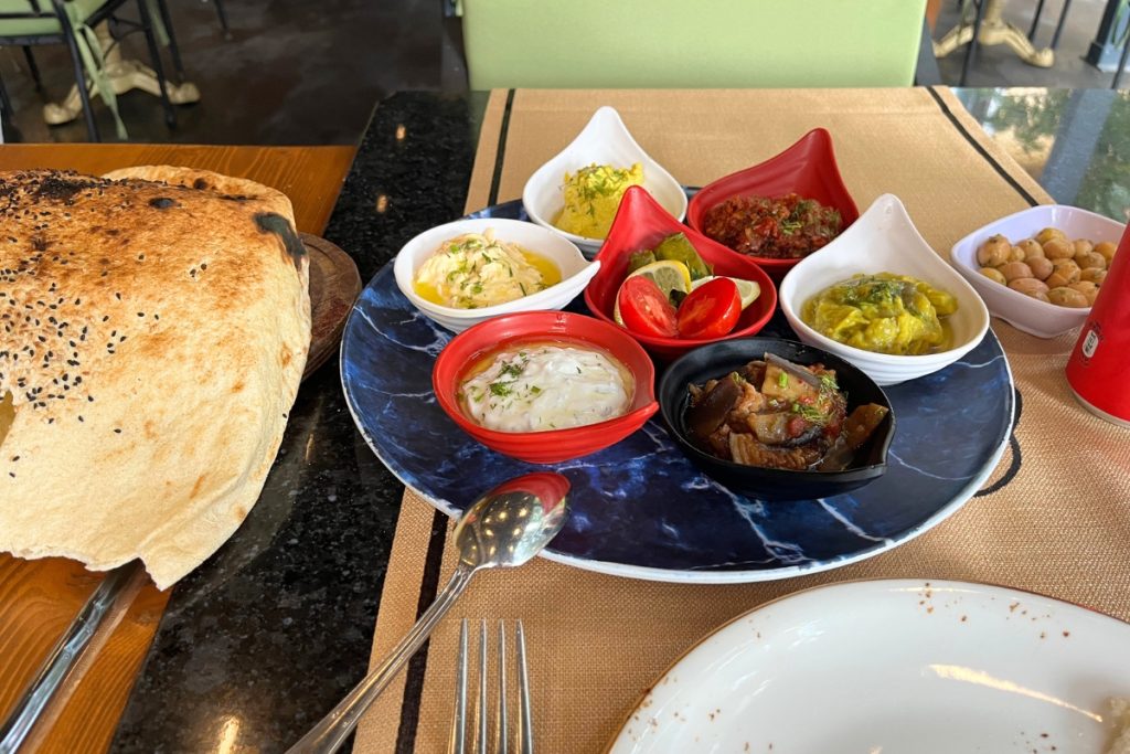 Turkish mezze spread on a round blue marble platter with red pepper dip, garlic yogurt sauce, stuffed grape leaves, olives, eggplant salad, and warm sesame flatbread.