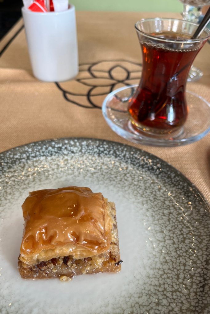 Slice of baklava on a plate next to a glass of Turkish tea in a tulip-shaped glass on a saucer.