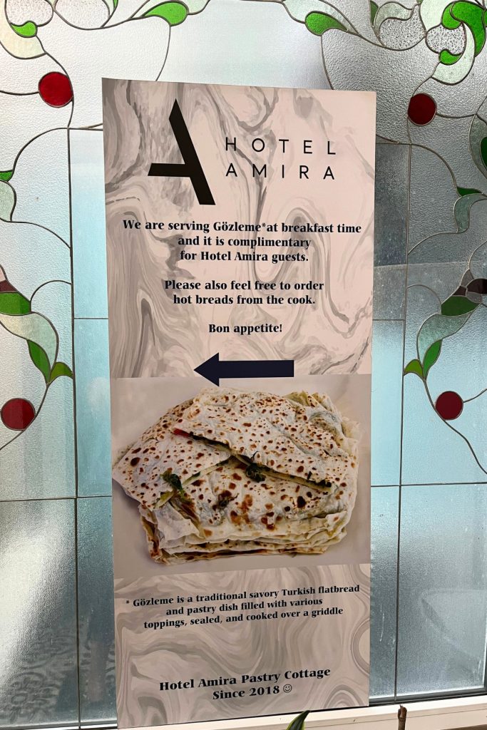 Sign for Hotel Amira Pastry Cottage advertising complimentary gözleme at breakfast, with a photo of the folded flatbread and stained glass decoration nearby.