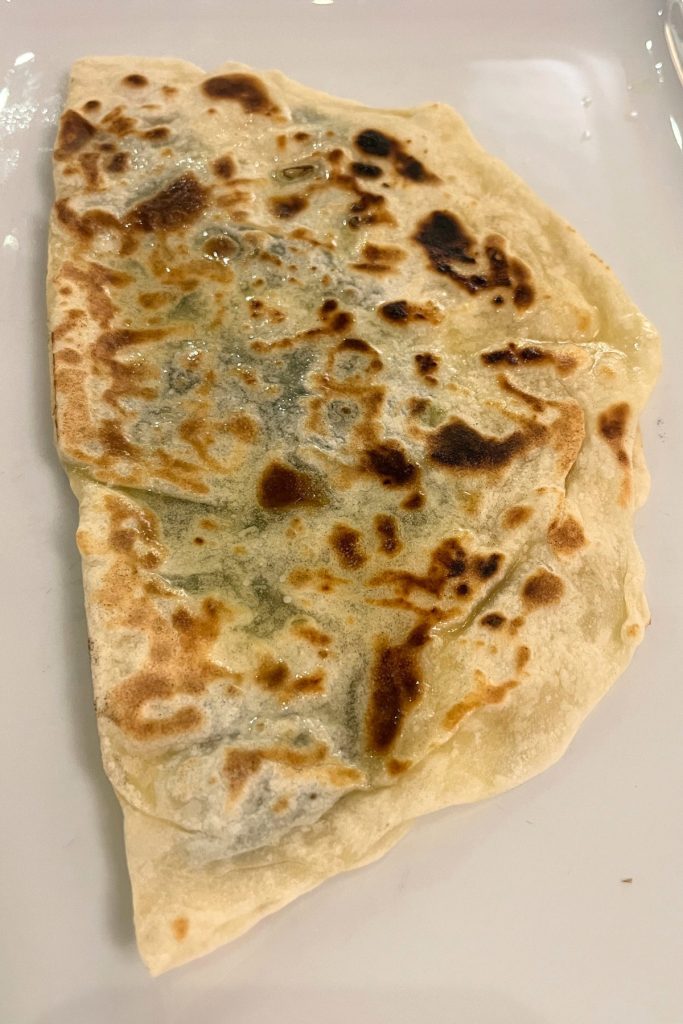Golden brown folded gözleme flatbread with visible spinach filling, served on a white rectangular plate.