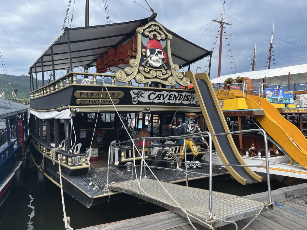 Pirate-themed tour boat named Cavendish with skull emblem and slide, docked in Paraty harbor