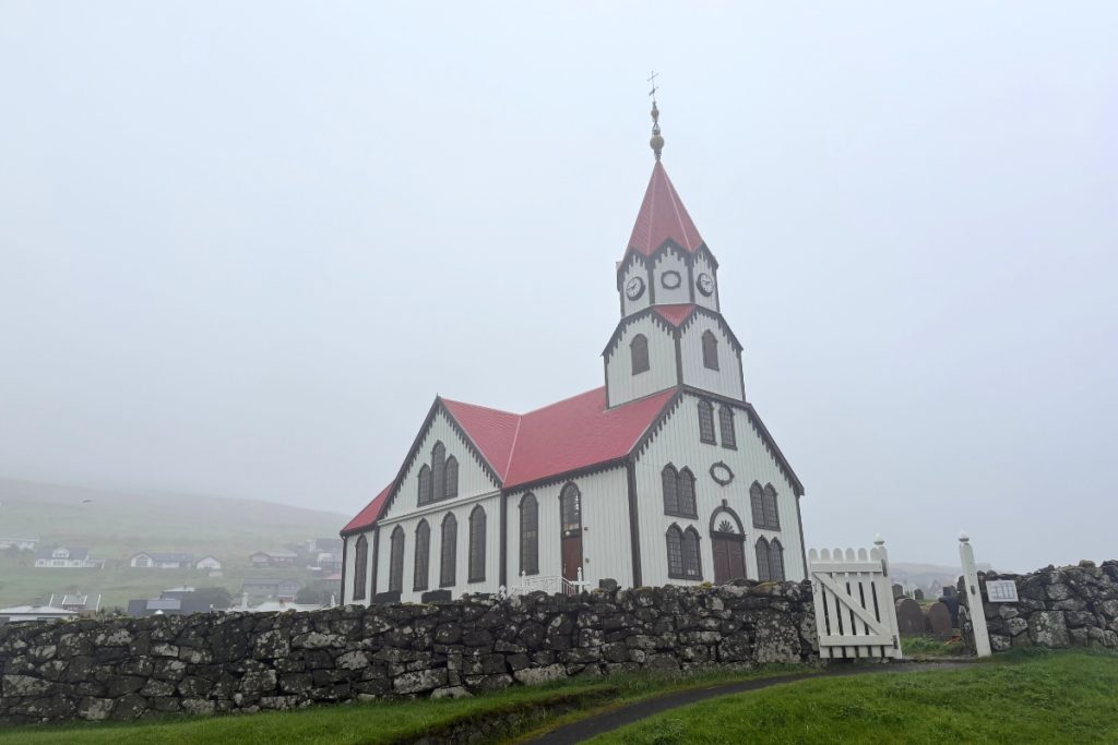 A white church with a red roof and tiered clock tower in Sandavágur, Faroe Islands
