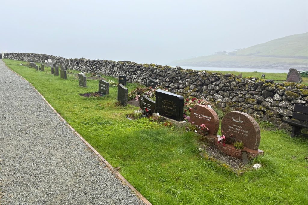 A cemetery bordered by a stone wall along the water in Sandavágur, Faroe Islands