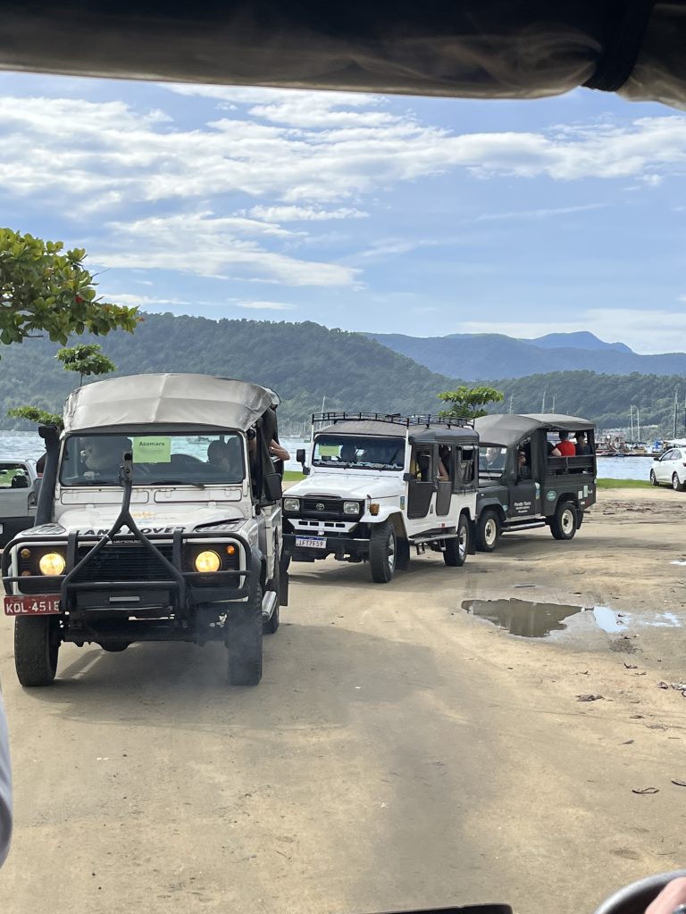 Convoy of open-air Land Rover 4x4 tour vehicles parked near Paraty harbor