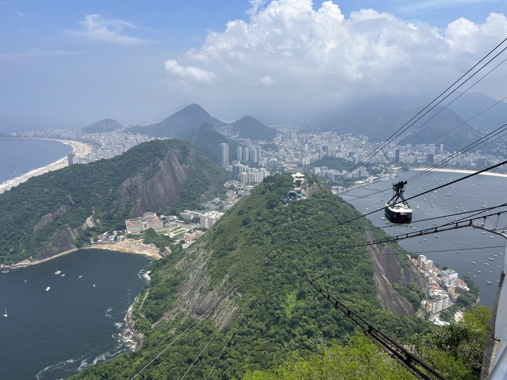 Aerial view from Sugarloaf Mountain of a cable car over Morro da Urca, with boats in the bay and the Rio de Janeiro coastline below