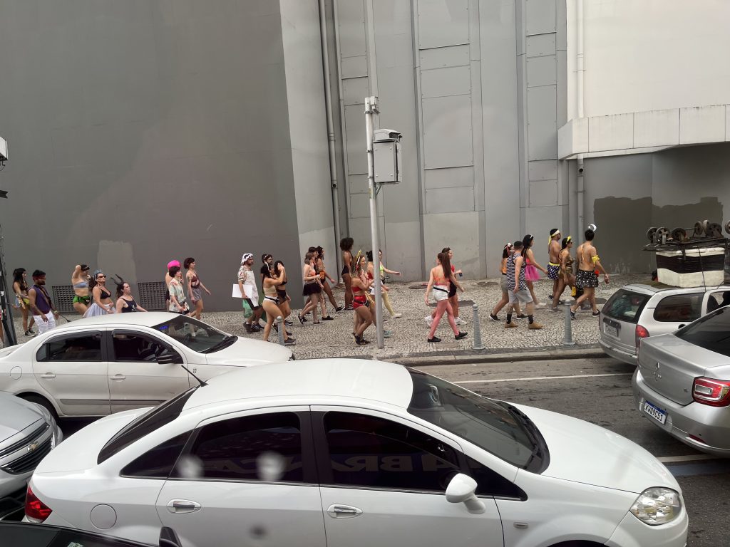 Costumed Carnival revelers crossing a Rio de Janeiro street, seen from a tour bus window in the morning